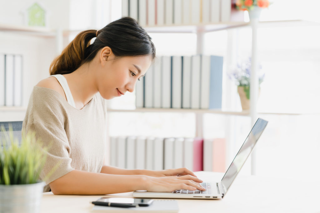 
young-smiling-asian-woman-working-laptop-desk-living-room-home